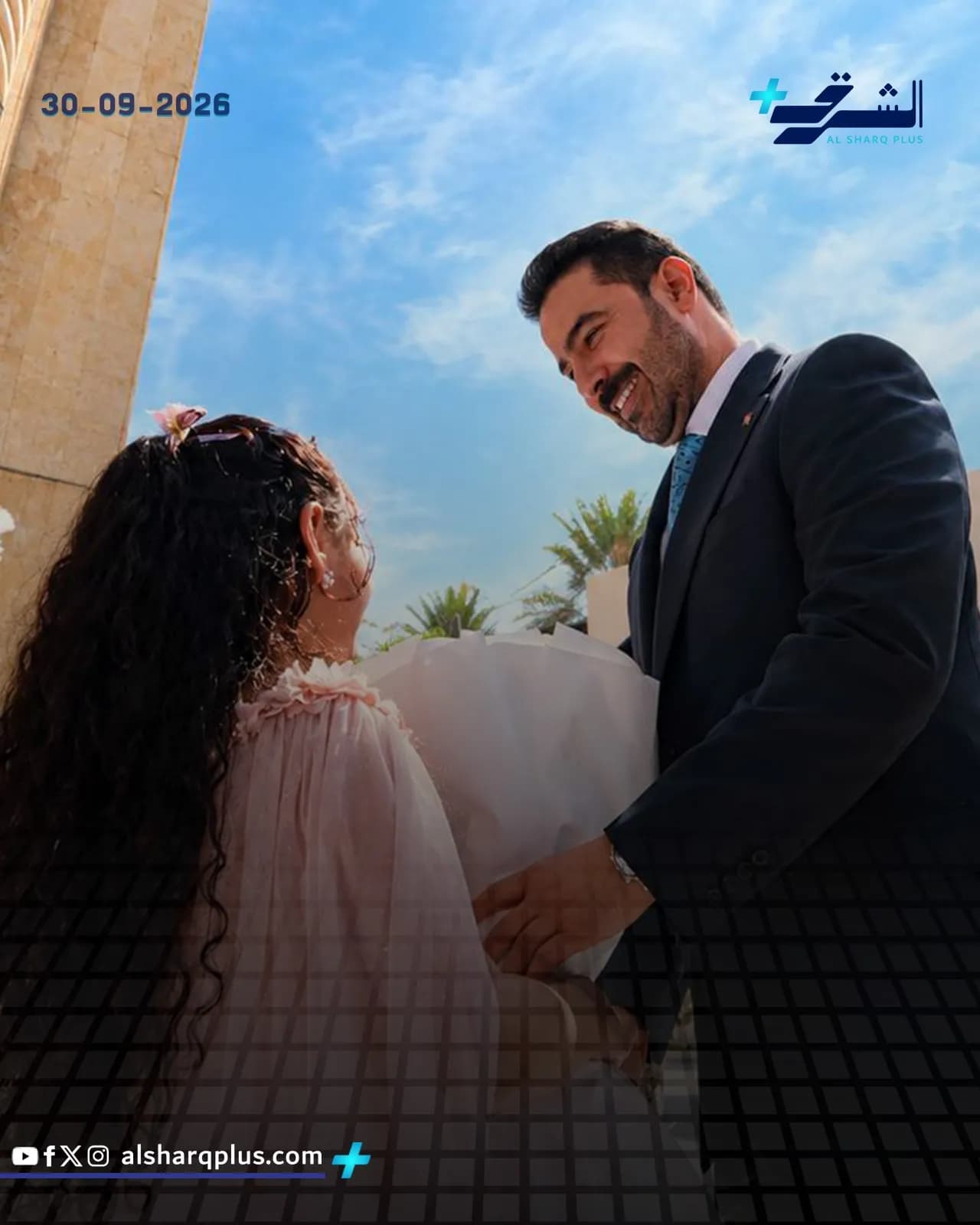 رجل يرتدي بدلة داكنة يبتسم لفتاة ذات شعر أسود كثيف ترتدي فستانًا ورديًا فاتحًا.