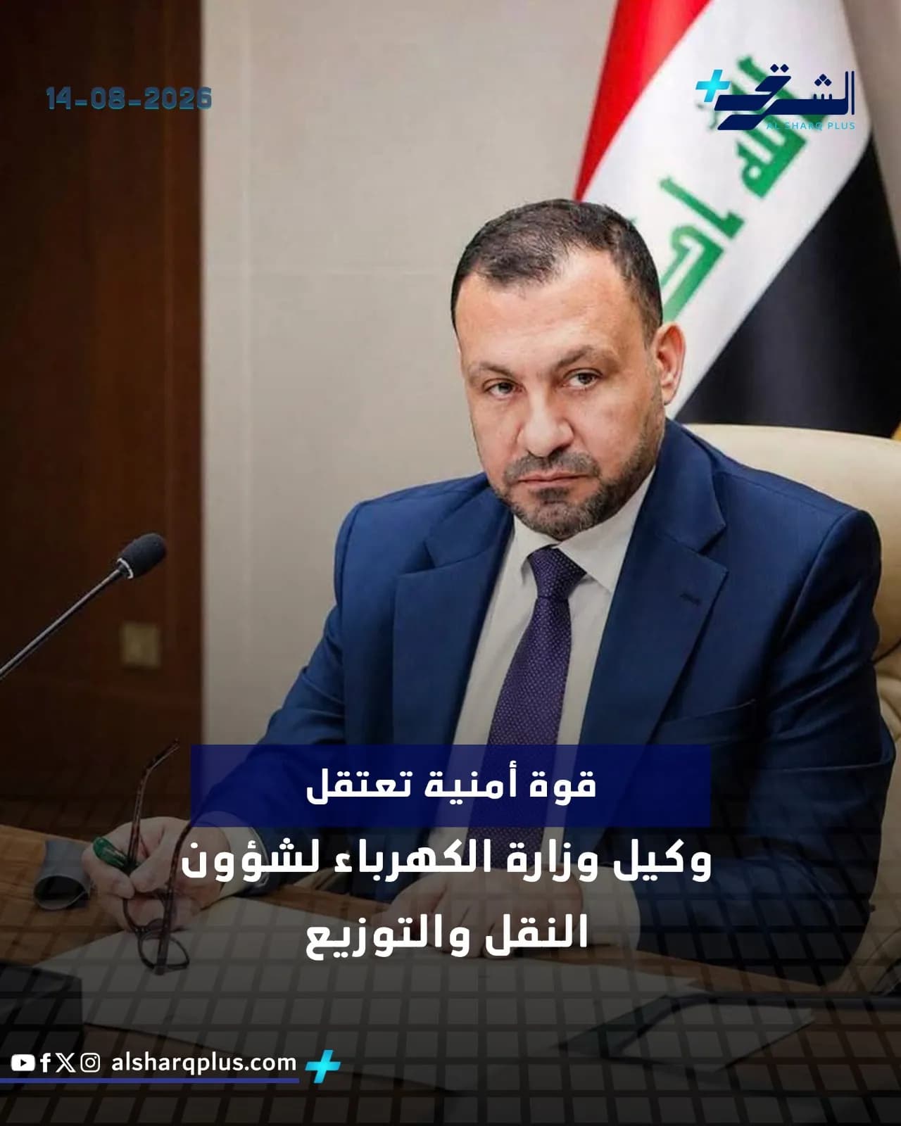 رجل يرتدي بدلة زرقاء وربطة عنق بنفسجية يجلس أمام علم العراق وميكروفون.