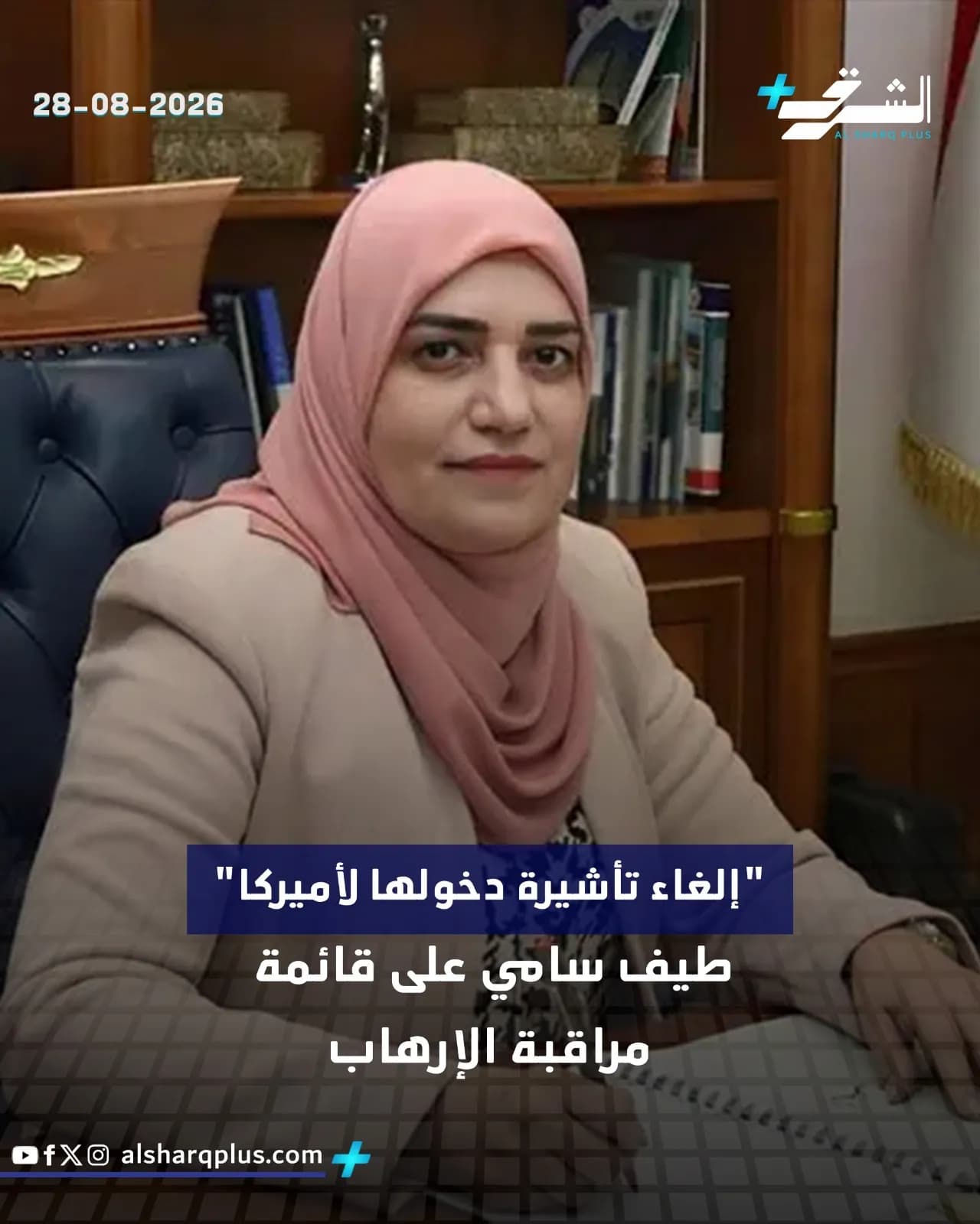 امرأة ترتدي حجابًا ورديًا وسترة بيج تجلس أمام مكتبة خشبية.