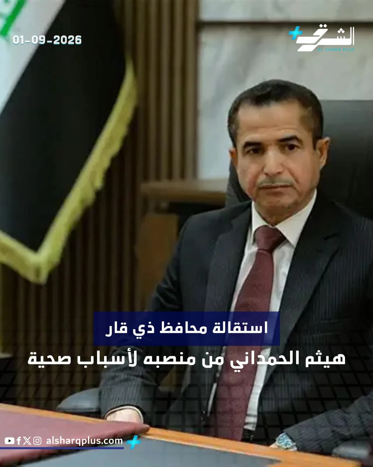 الشيخ هيثم الحميداني يرتدي بدلة داكنة وربطة عنق حمراء، ويجلس أمام علم العراق.