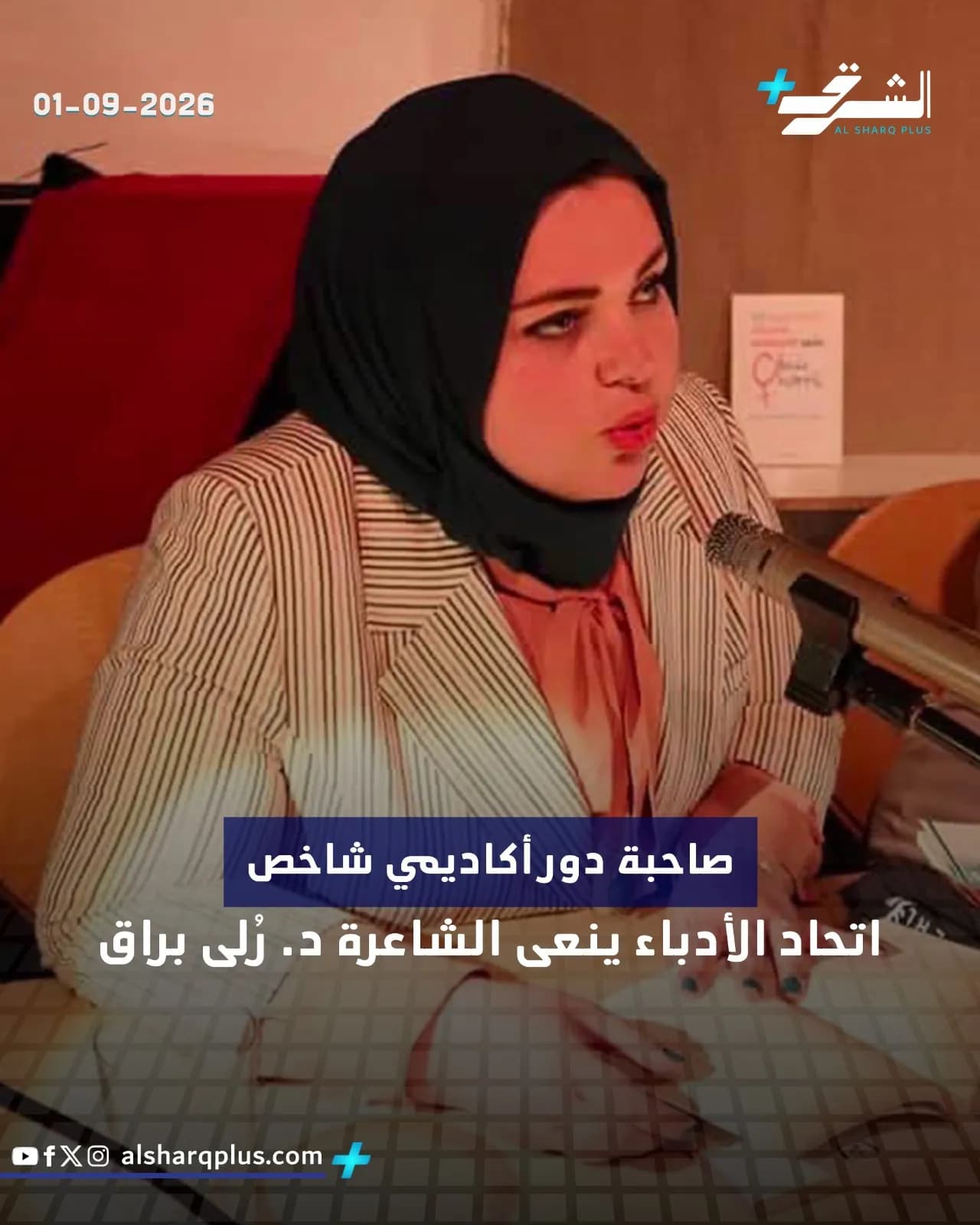 امرأة ترتدي حجابًا أسود وسترة مخططة تتحدث أمام ميكروفون، مع نص عربي على الشاشة.