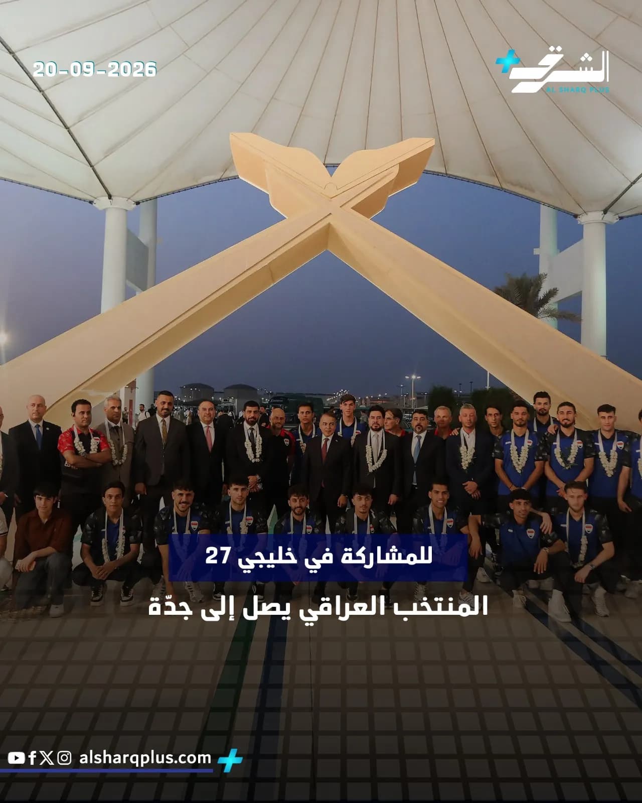 فريق كرة قدم عراقي يرتدي زيًا رياضيًا أزرق يقف لالتقاط صورة جماعية مع مسؤولين تحت مظلة عملاقة.