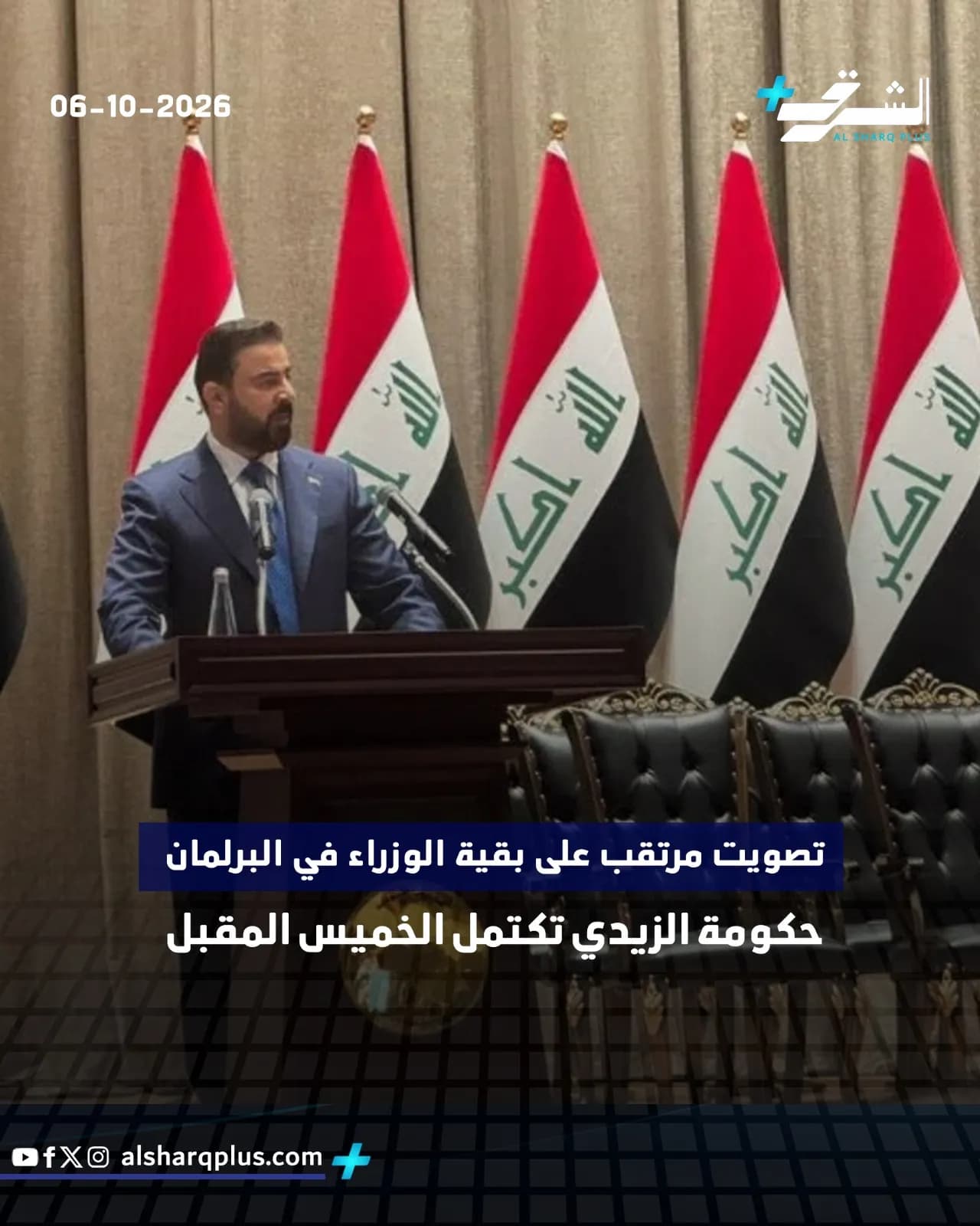 رجل يقف أمام منصة خطابة محاطًا بأربعة أعلام عراقية، وشعار محطة إخبارية وتاريخ في الأعلى.