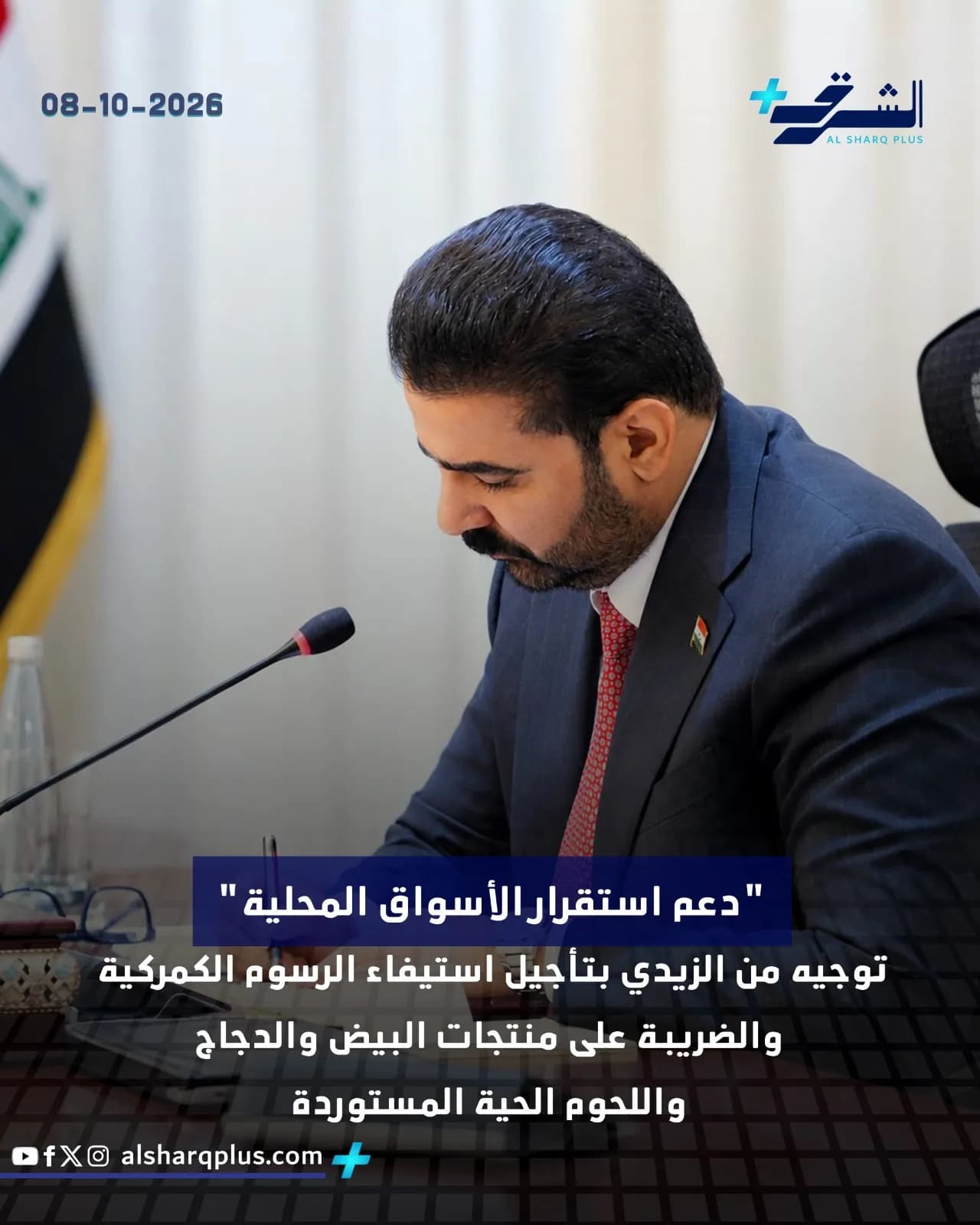 رجل يرتدي بدلة داكنة وربطة عنق حمراء يتحدث إلى ميكروفون، مع لافتة إعلامية في الأسفل.