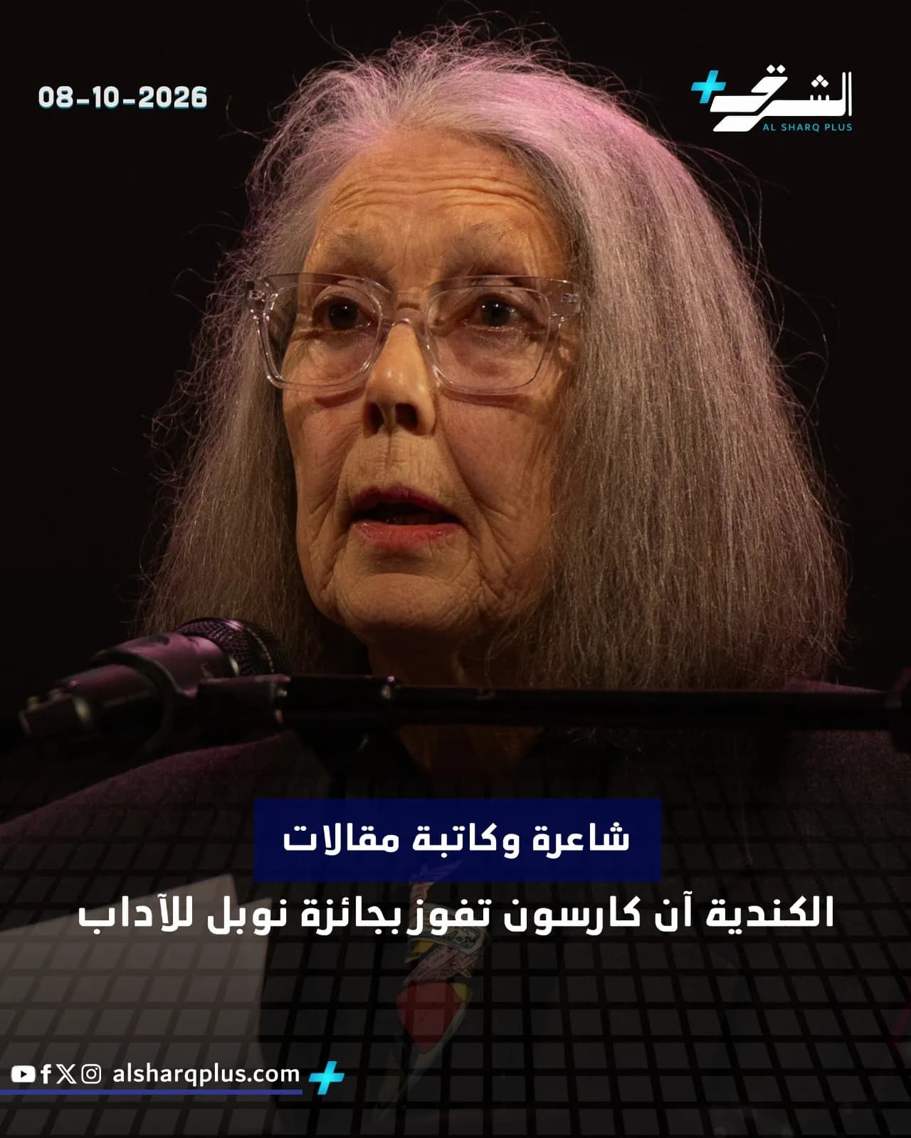 صورة مقربة لامرأة عجوز ترتدي نظارات، بشعر رمادي طويل، تتحدث خلف ميكروفون، مع نص عربي على الشاشة.