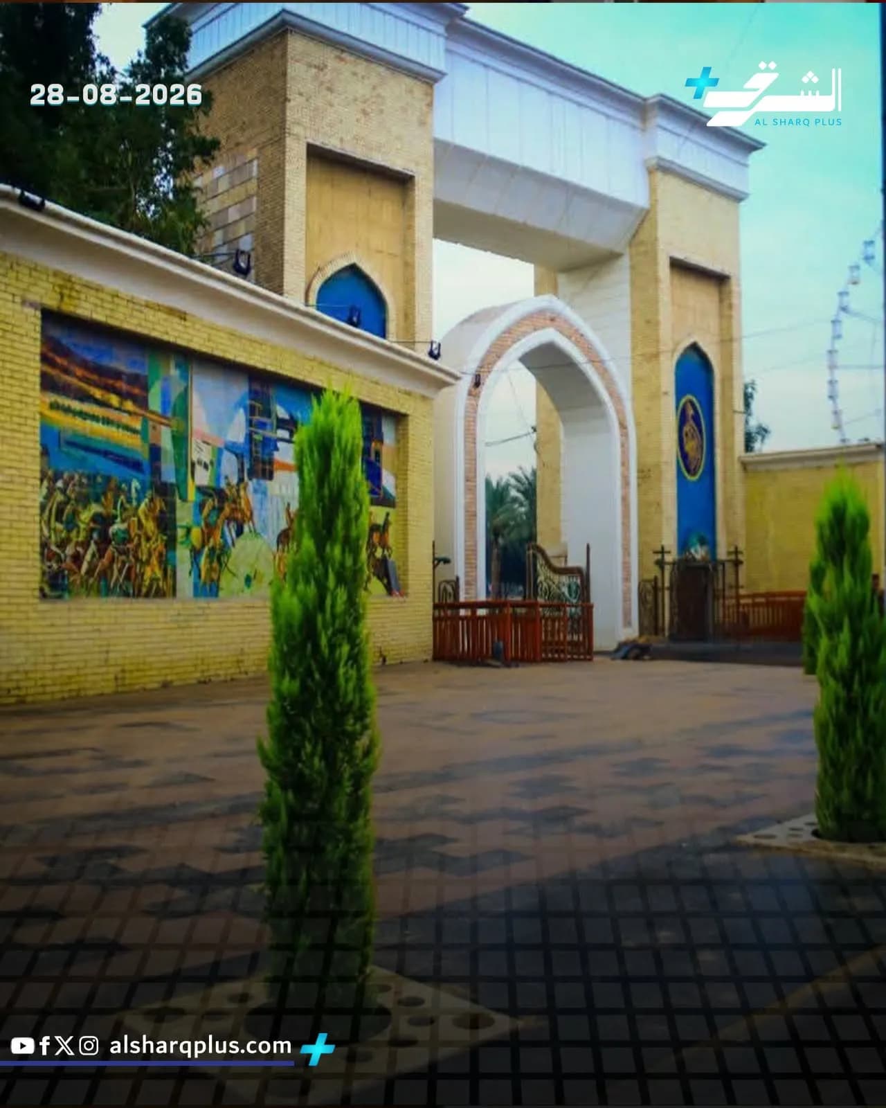 تظهر لقطة خارجية لمبنى بمدخل مقوس وبجواره لوحة جدارية كبيرة، وعلى الأرض نباتات خضراء.