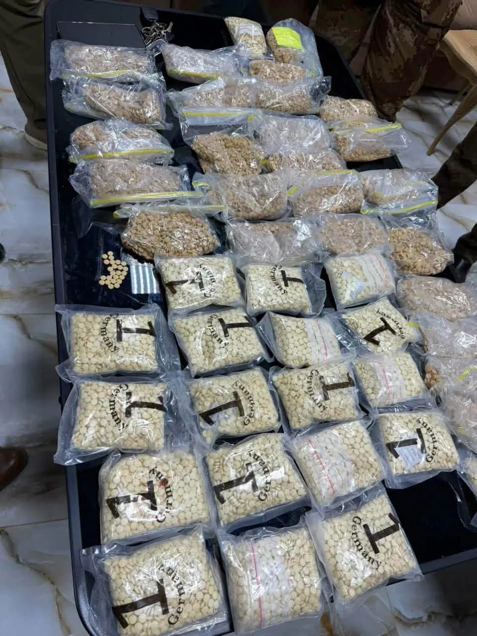 كمية كبيرة من الحبوب المخدرة والماريجوانا في أكياس بلاستيكية، معروضة على طاولة سوداء.
