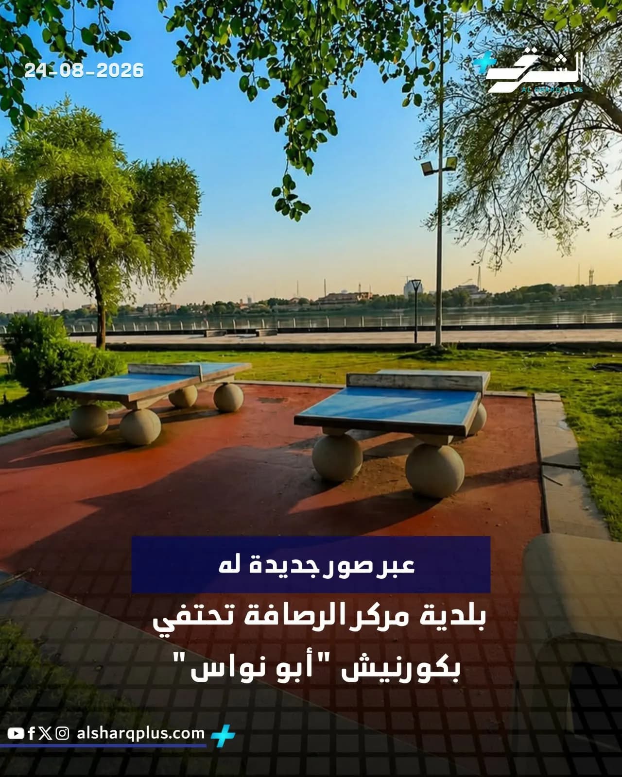 طاولات تنس طاولة في حديقة خضراء على ضفة نهر، وتحيط بها الأشجار تحت سماء زرقاء صافية.