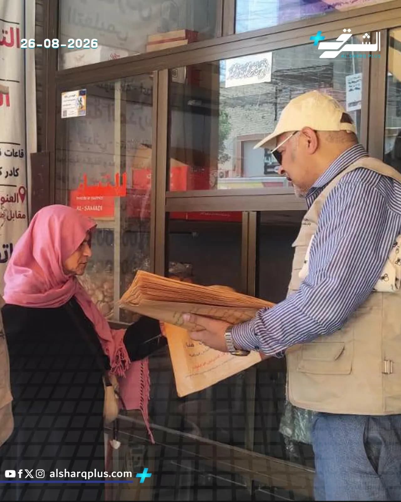 امرأة محجبة تستلم مستندات ورقية من رجل يرتدي قبعة وسترة في مكان يشبه مكتبًا حكوميًا.