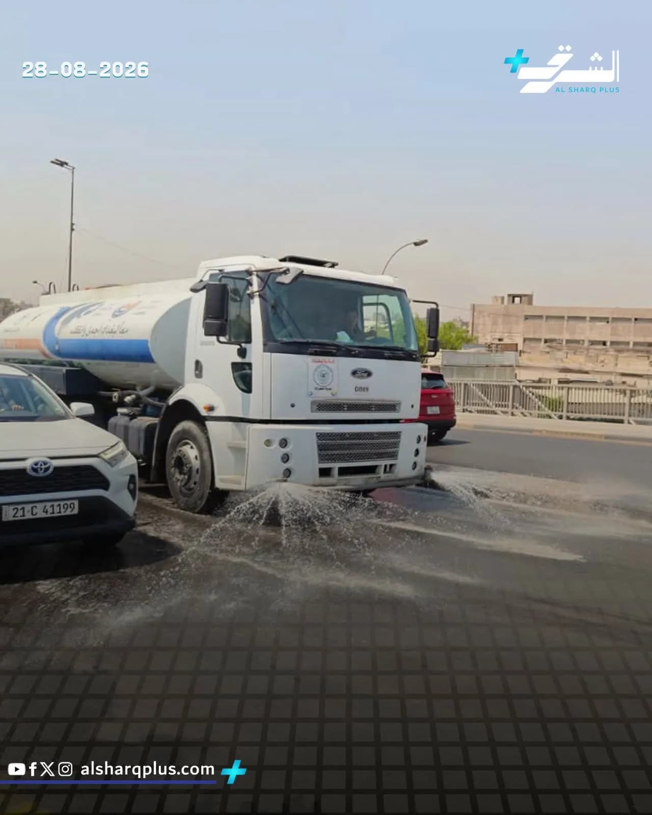 شاحنة صهريج بيضاء ترش الماء لتنظيف طريق مبلط بالأسفلت.