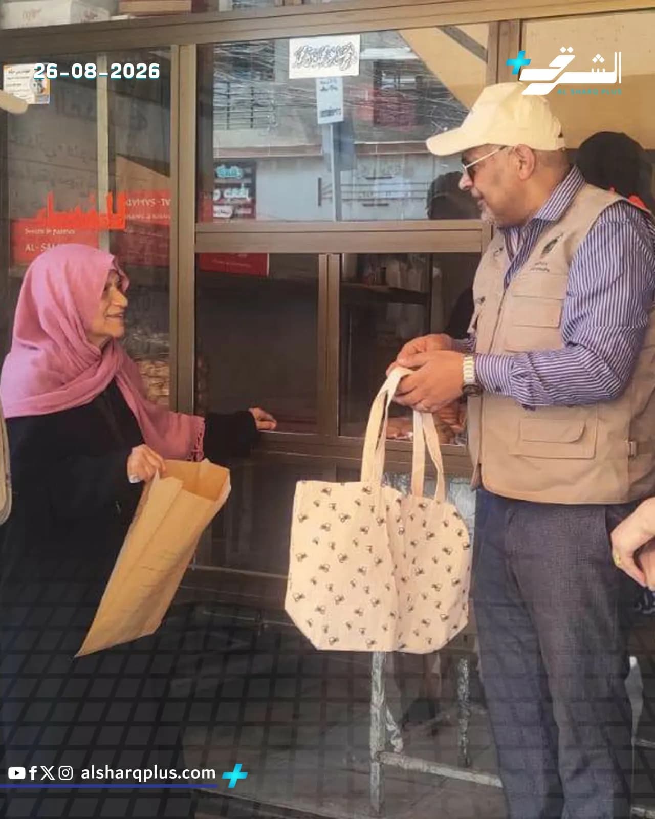 رجل يرتدي قبعة بيج وسترة فاتحة يعطي حقيبة قماشية لامرأة ترتدي حجابًا ورديًا وحجابًا أسود.